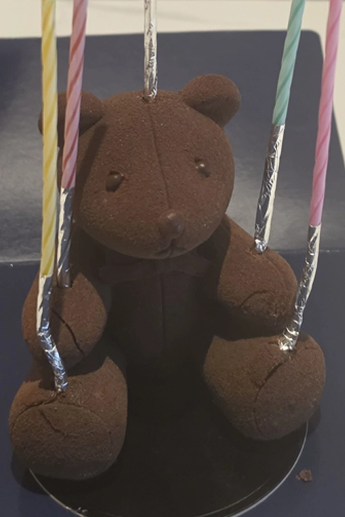 생일 축하를 위해 팔과 다리 쪽에 초를 꽂은 곰 모양 초콜릿